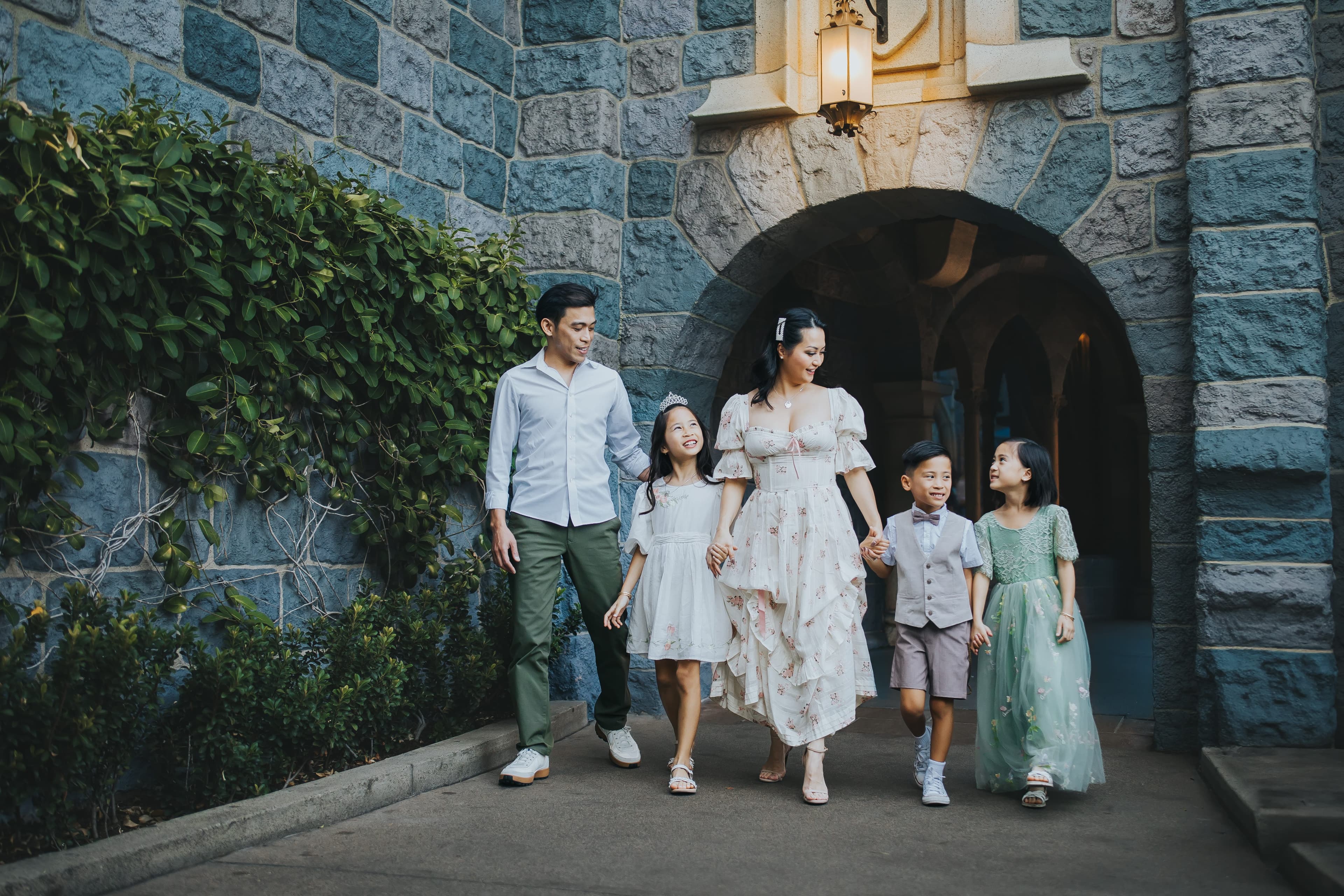 A family of five walks hand in hand beneath a stone archway.